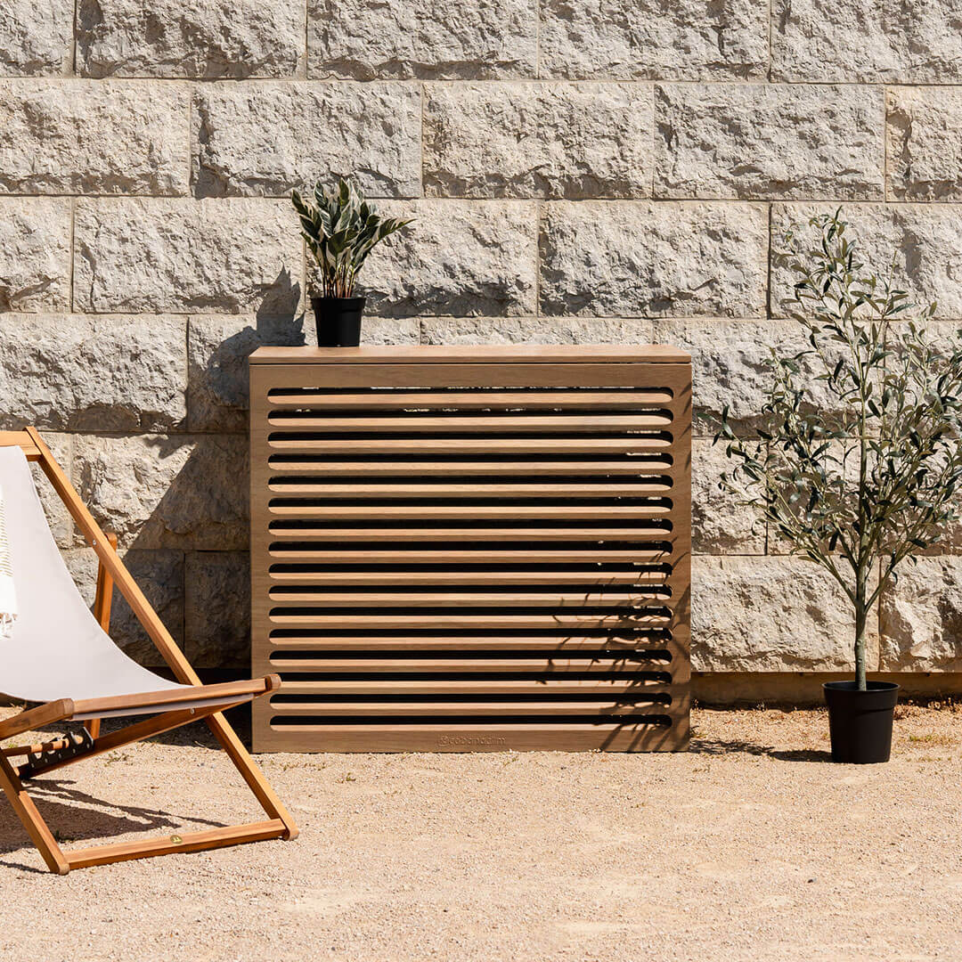Cache clim bois exotique – taille L, installé avec soin – vue de face avec déco. Structure ventilée et design, idéale pour sublimer une façade ou un jardin. Un rendu soigné qui allie déco et performance.