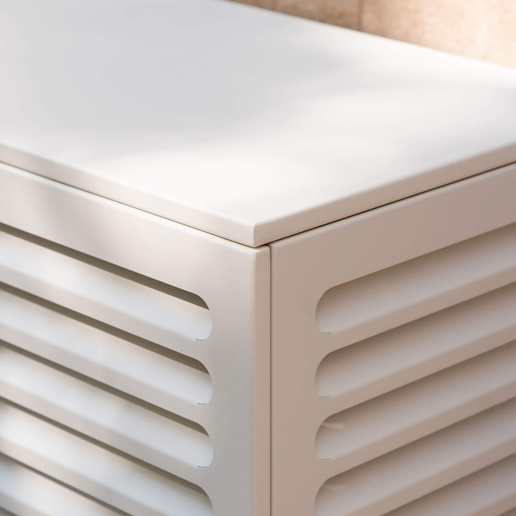 Cache clim blanc crème (RAL 9010) pour climatiseur ou pompe à chaleur – vue d’angle zoomée sur fond de mur clair, aluminium thermolaqué avec persiennes, protection esthétique et durable pour unité extérieur